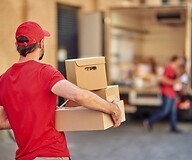 A man in a courier outfit carries parcels to a delivery van.