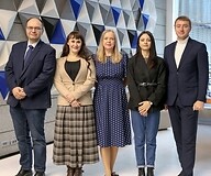 Five people in business attire pose for a photograph in an office space