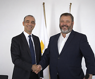 Two men in suits with the Cypriot and Polish flags in the background
