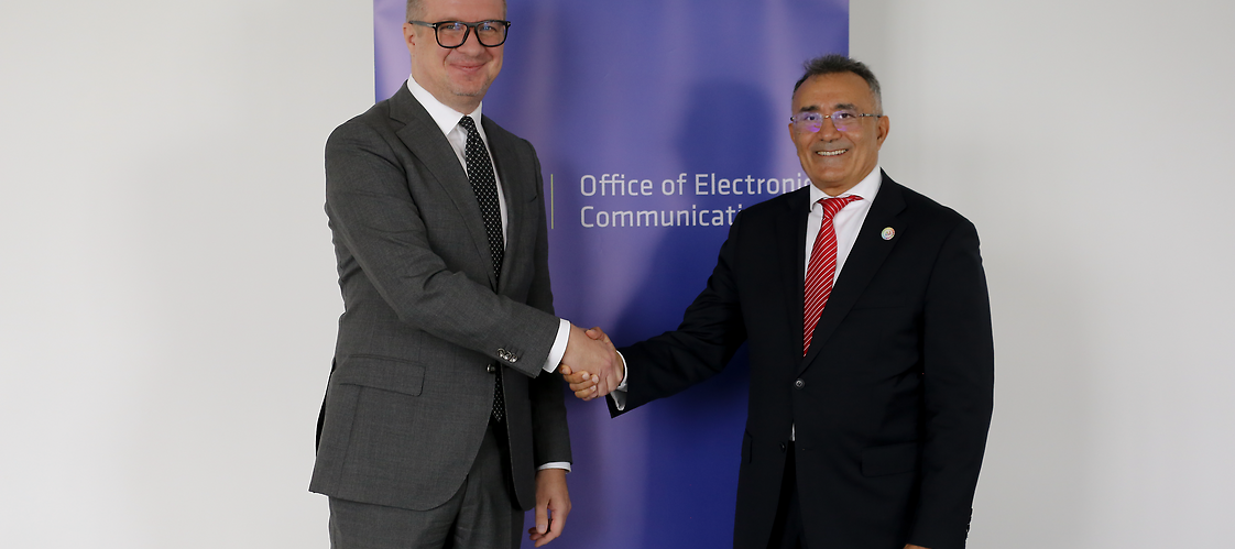 Two men in suits are shaking hands; a roll-up banner with the UKE logo is visible in the background.