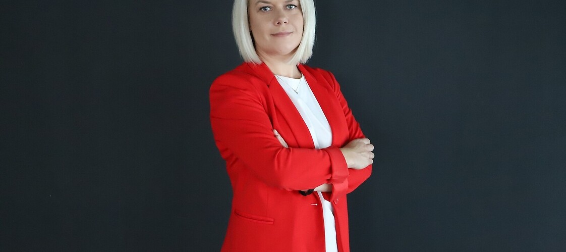 KOnbieta w czerwonym żakiecie i białej bluzce na ciemnym jednolitym tle