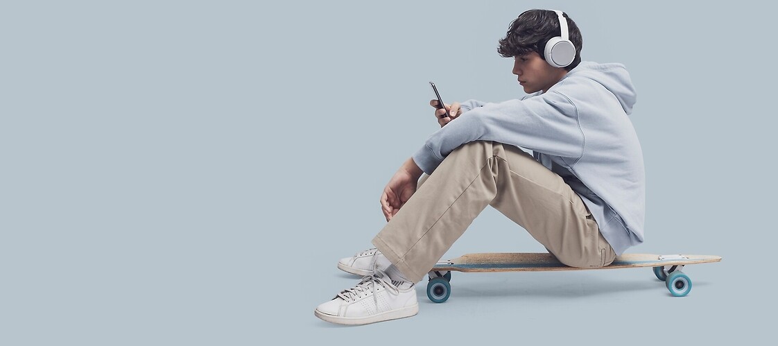 Nastolatek siędzący na deskorolce patrzy w smartfon