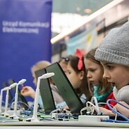 Grupa dzieci przed komputerami i makietą miasta na tle baneru UKE