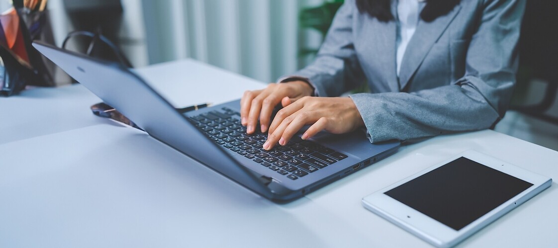 Dłonie kobiety na klawiaturze komputera, obok tablet