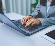 Dłonie kobiety na klawiaturze komputera, obok tablet