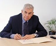 Męzczyzna w garniturze za stołem podpisuje dokument