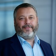 Mężczyzna w ciemnej marynarce i jasnej koszuli na tle biurowego wnętrza