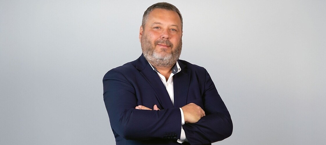 Mężczyzna w garniturze i białej koszuli, z założonymi rękami na białym tle