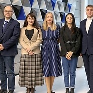 Pięć osób w ubraniach biznesowych pozuje do zdjęcia w przestrzeni biurowej