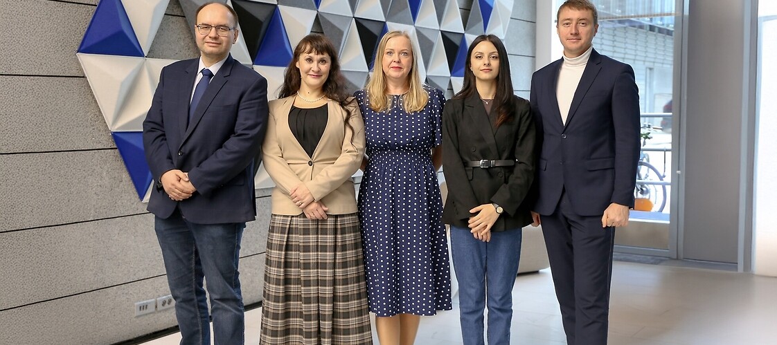Pięć osób w ubraniach biznesowych pozuje do zdjęcia w przestrzeni biurowej