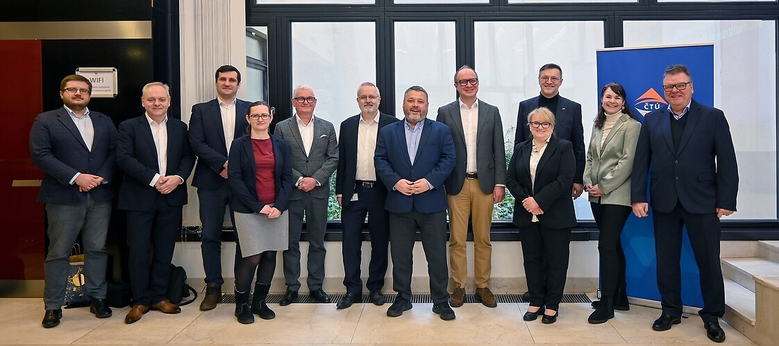 Grupa kilkunastu osób w strojach biznesowych w przestrzeni biurowej pozuje do zbiorowego zdjęcia