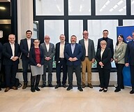 Grupa kilkunastu osób w strojach biznesowych w przestrzeni biurowej pozuje do ...