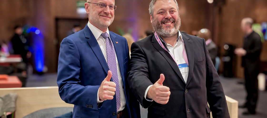 Dwóch uśmiechniętyvh męzczyzn w garniturach w przestrzeni konferencyjnej