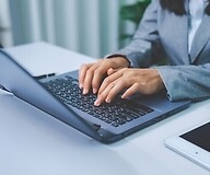 Dłonie na klawiaturze laptopa, obok telefon komórkowy
