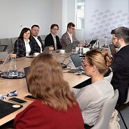 Grupa kilku osób w strojach biznjesowych po obu stronach stołu konferencyjnego