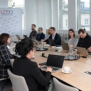 Grupa kilku osób w strojach biznjesowych po obu stronach stołu konferencyjnego