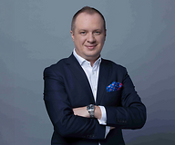 Mężczyzna w garniturze z założonymi rękami, na ciemnym jednolitym tle